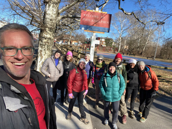 Self portrait of JJ w/ crowds of walkers in front of "Welcome to Philadelphia" sign